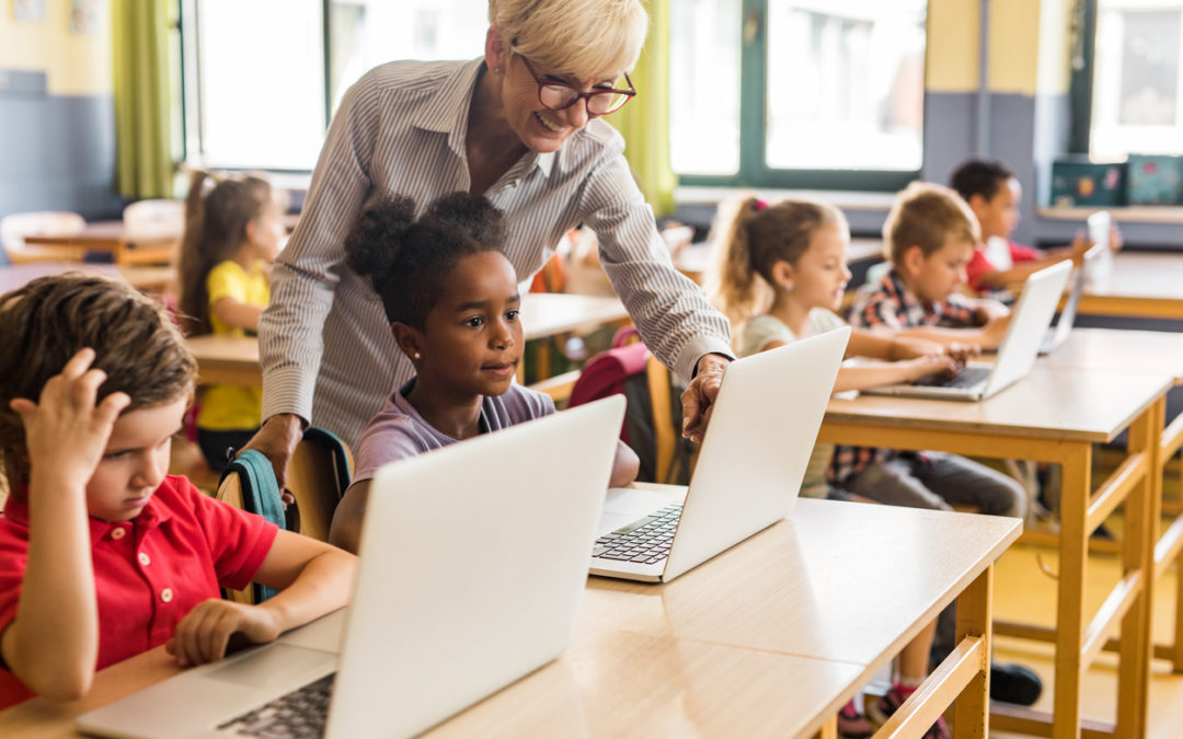 Teacher instructing keyboarding in students at desks in classroom with laptops